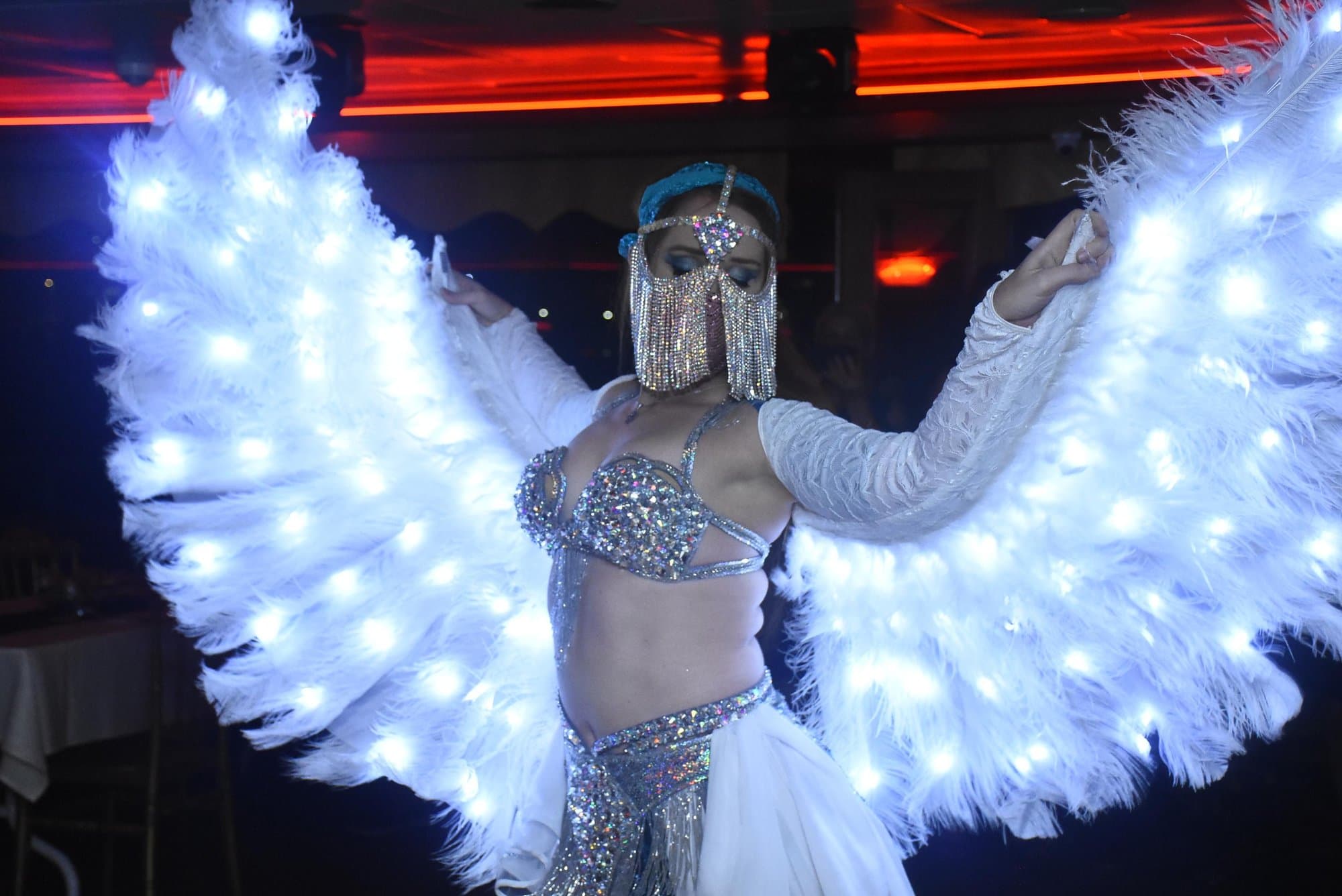 A belly dancer performing with illuminated white feather wings on the cruise