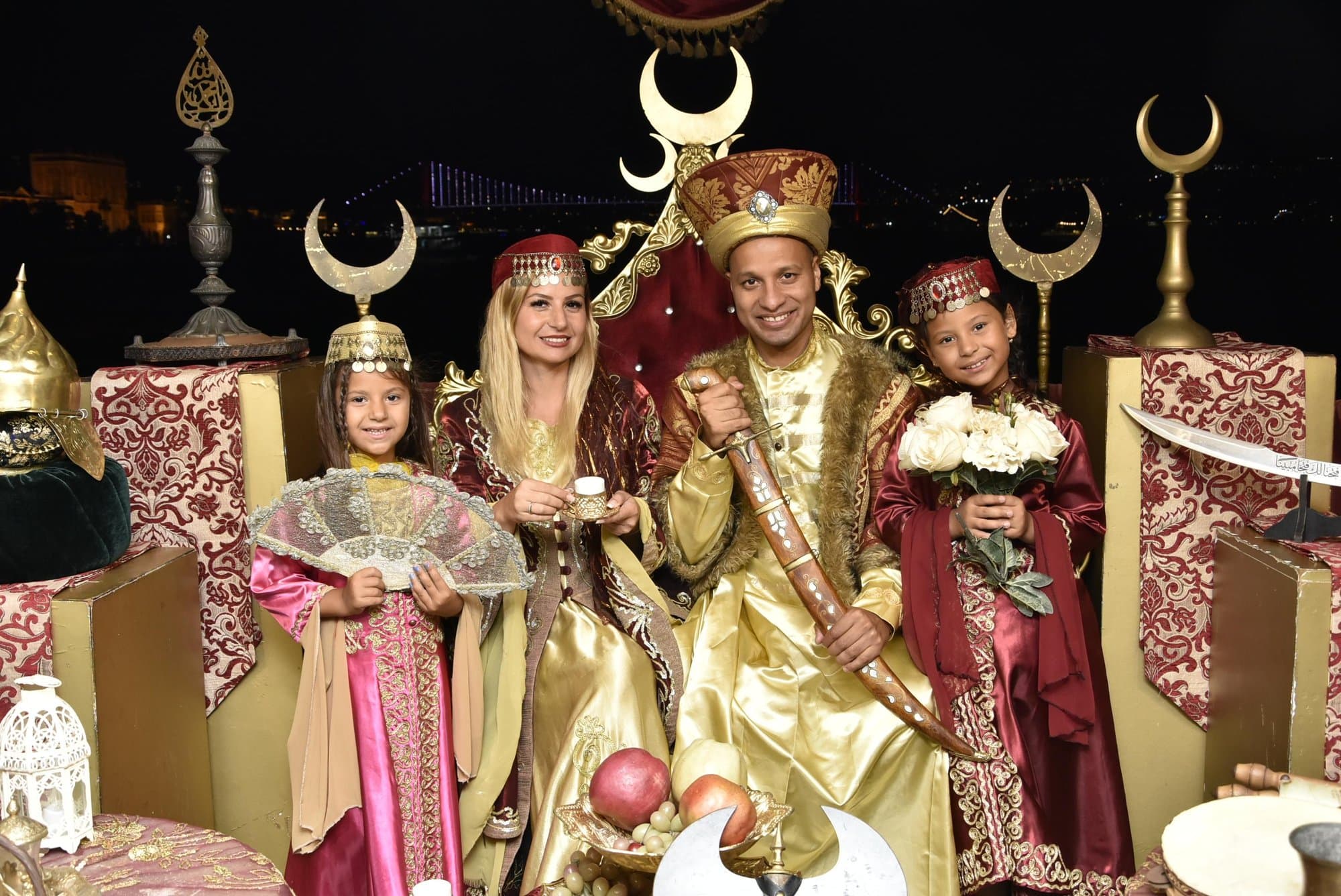 Guests posing in Ottoman costumes on a throne with the Bosphorus skyline at night behind