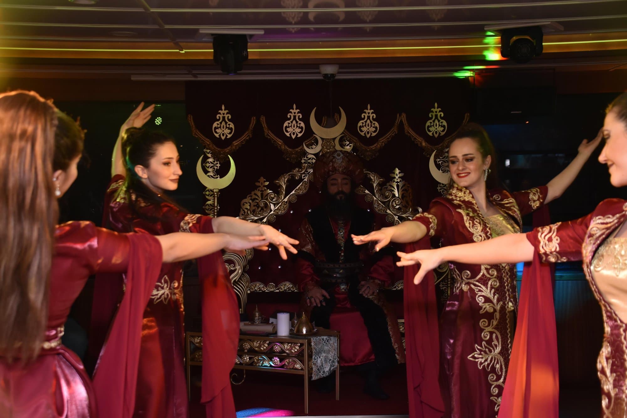 Dancers in red Ottoman costumes performing in front of a sultan's throne on the dinner cruise