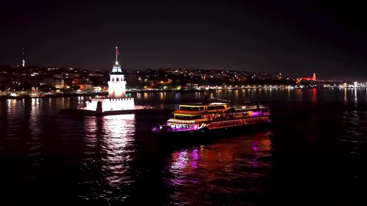 A Bosphorus dinner cruise boat lit up at night passing the Maidens Tower with the Istanbul skyline