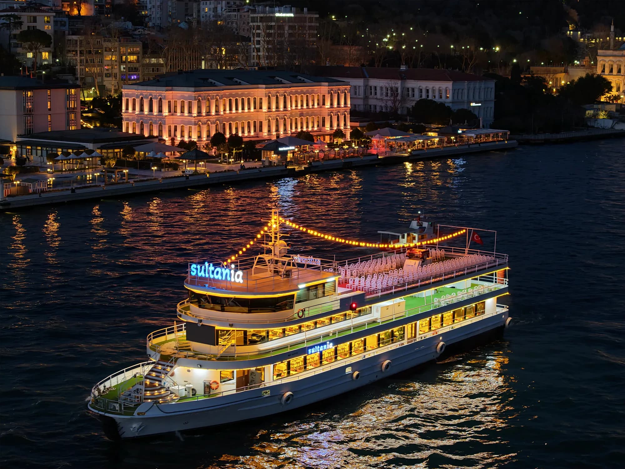 A dinner cruise boat lit up at night on the Bosphorus by the Çırağan Palace