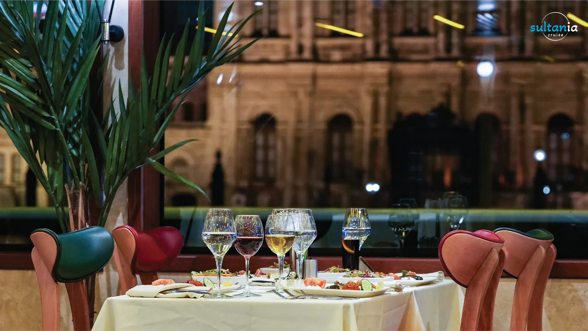 A set dinner table on the boat with an illuminated Ottoman palace through the window at night