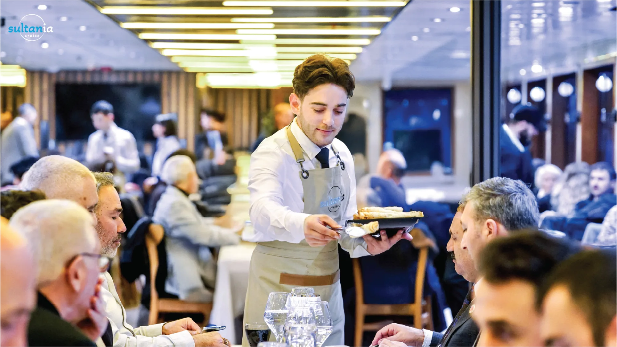 A waiter serving guests at their tables in the boat's dining lounge