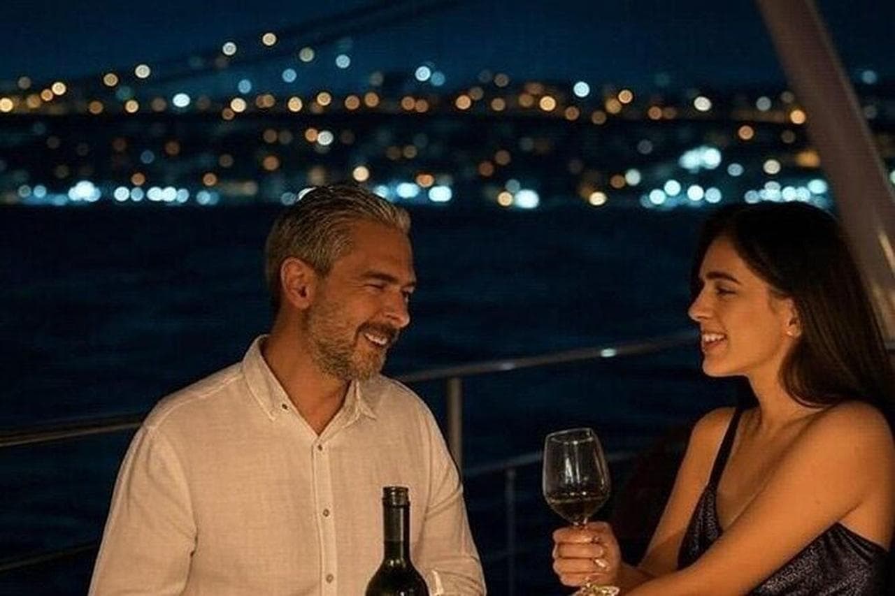 A couple with a glass of wine on deck as the city lights glow behind