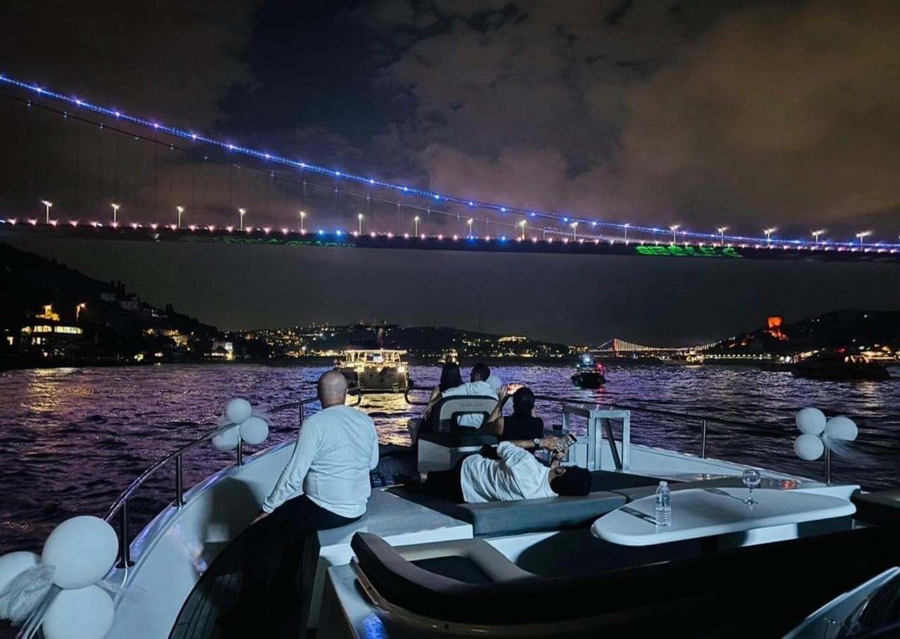 Guests on the luxury yacht's deck at night with the lit Bosphorus Bridge ahead