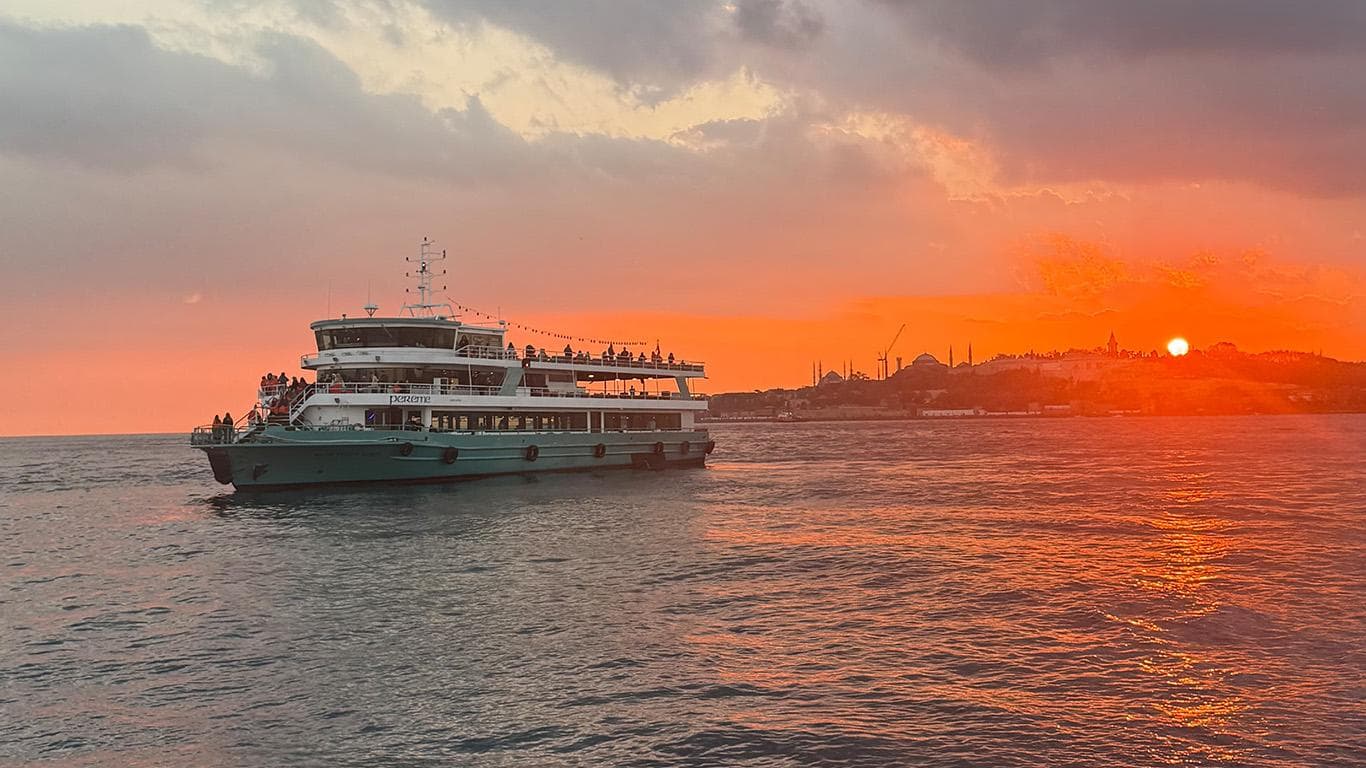 The Pereme boat on the Bosphorus at sunset with the historic Istanbul skyline and the setting sun behind