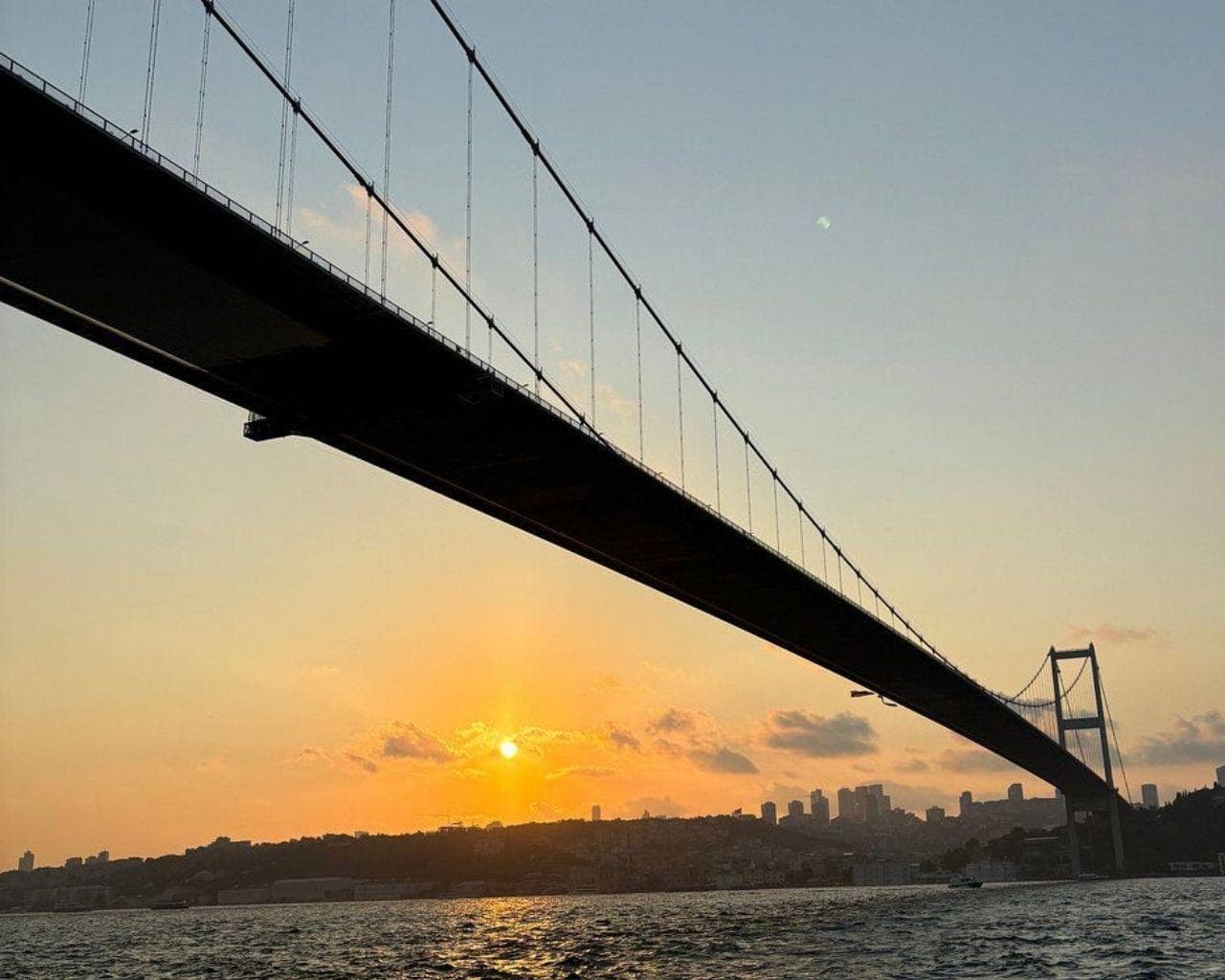 The Bosphorus Bridge seen from the water as the sun sets over the city