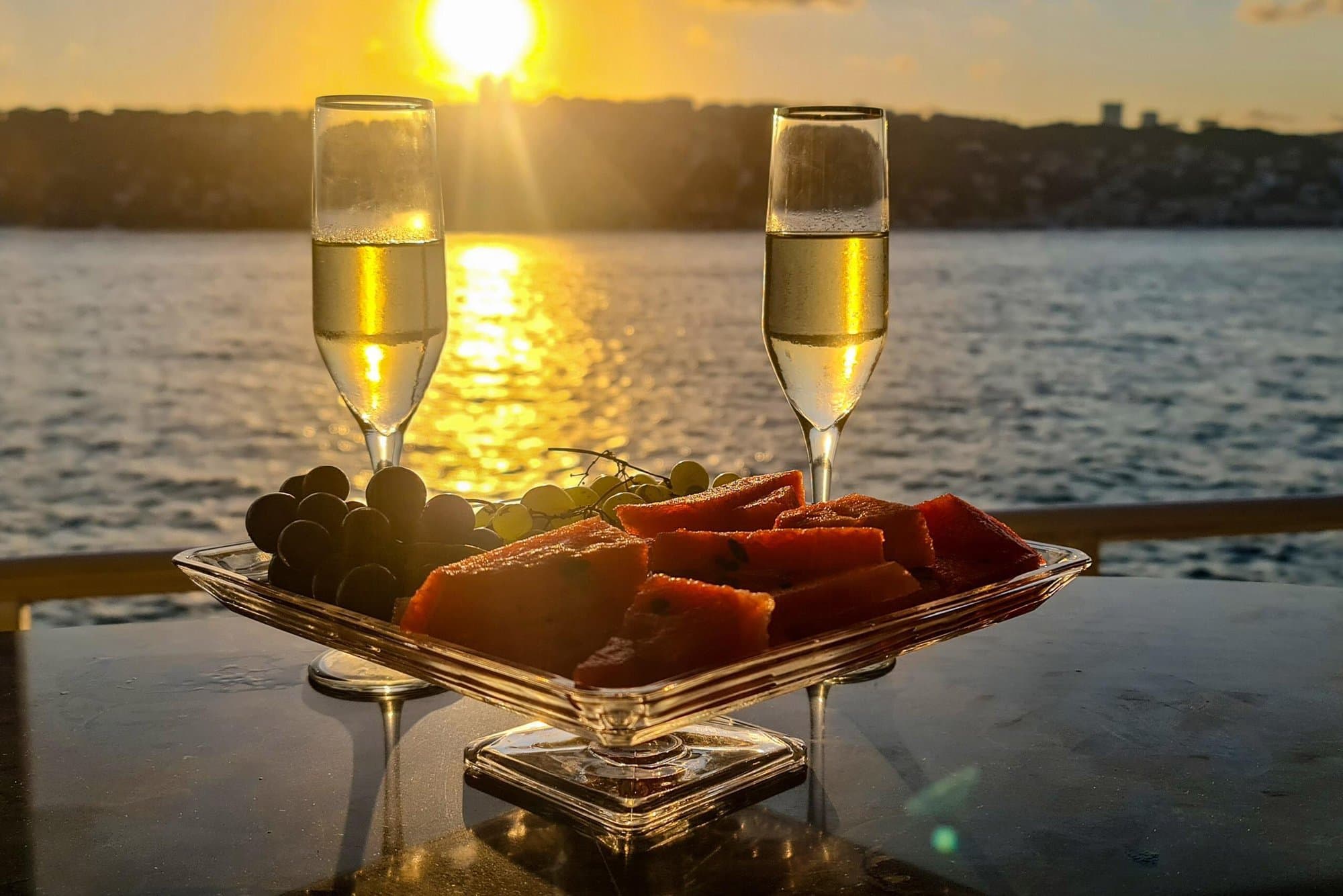 A plate of fresh fruit and two glasses on the deck table with the golden Bosphorus sunset behind