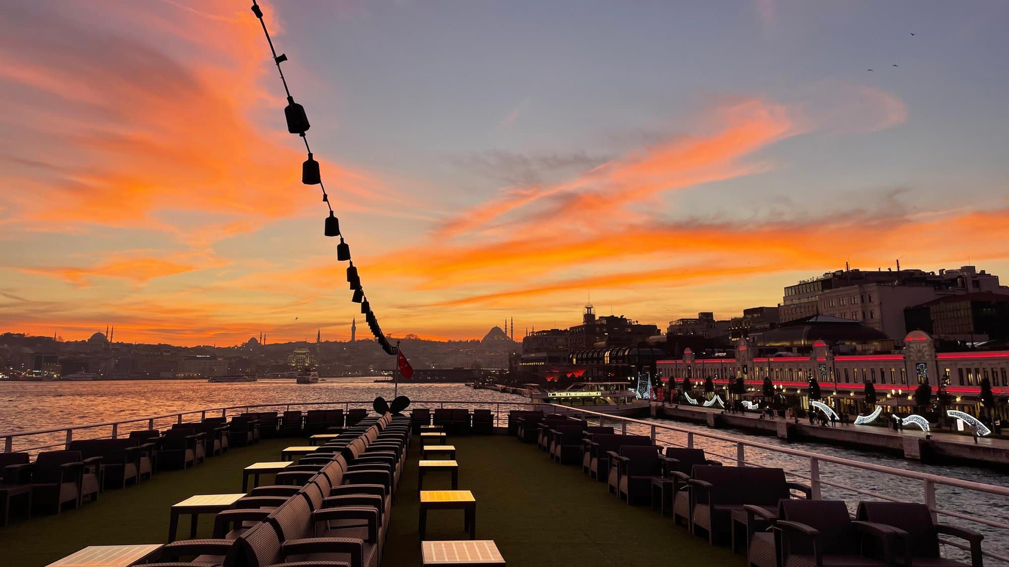 The open-deck lounge seating at dusk as the boat passes the illuminated Eminönü waterfront