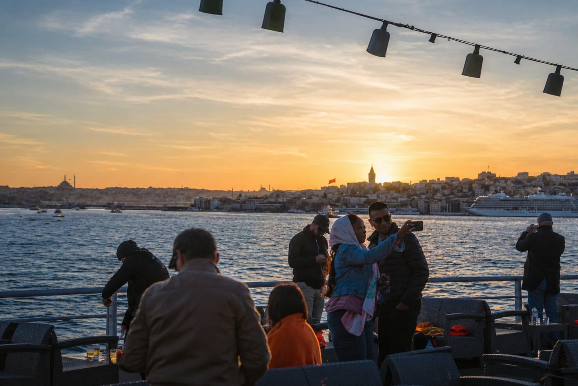 Passengers taking photos on deck with the Galata Tower silhouetted against the sunset