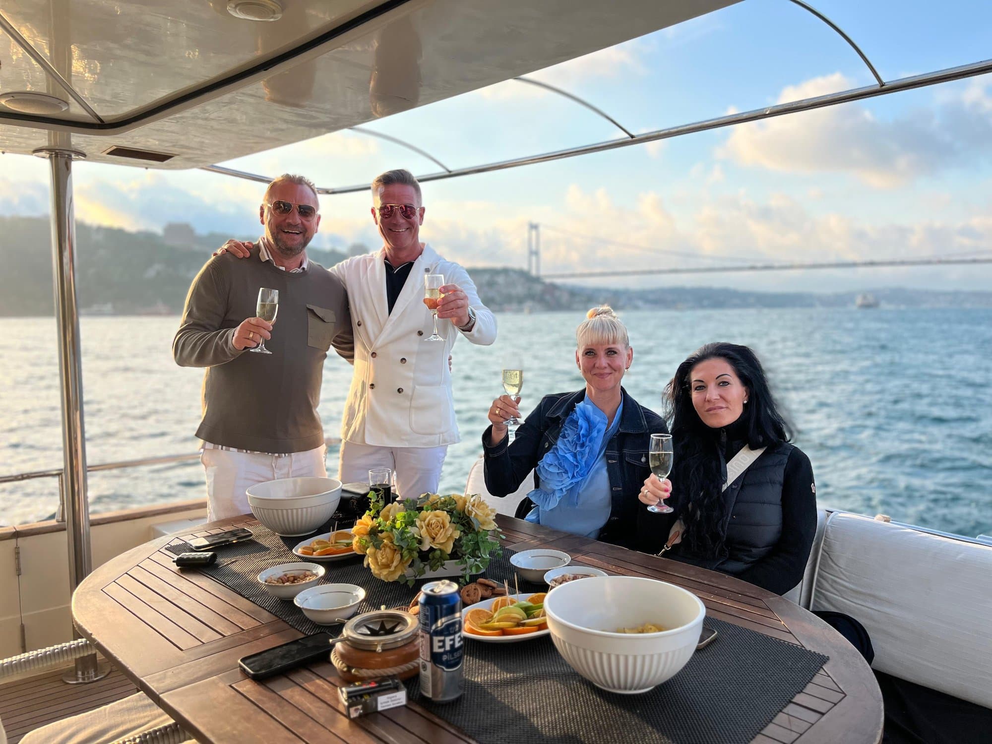 Guests toasting drinks at a table on the yacht with the Bosphorus Bridge behind