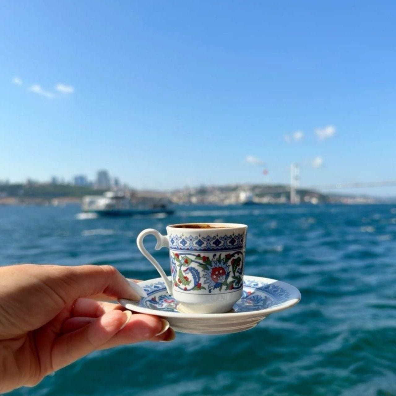 A cup of Turkish coffee held up with the Bosphorus Bridge behind